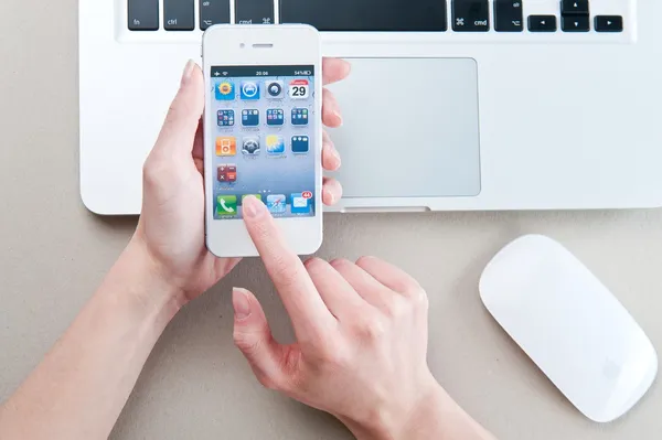 White iphone 4 in womans hands next to macbook pro — Stock Photo, Image