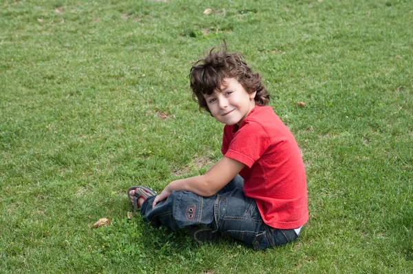 Criança feliz sentada na grama — Fotografia de Stock