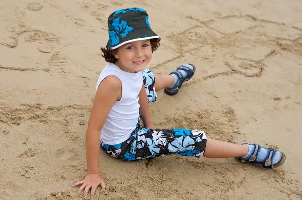 Милый мальчик, сидящий на песке с пляжа — стоковое фото