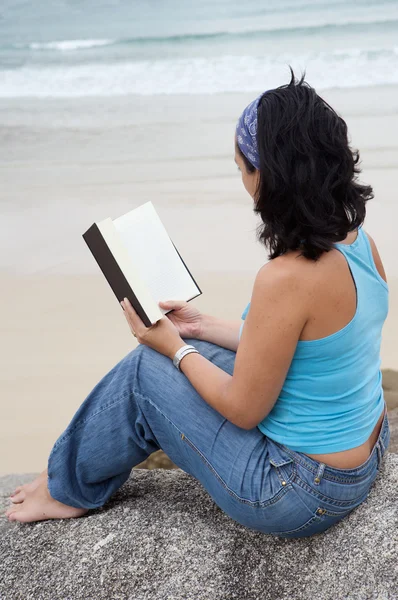 Jonge vrouw lezen zittend op het strand — Stockfoto