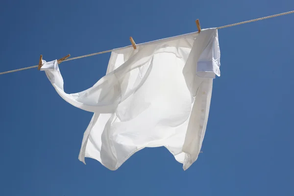Camisa blanca lavada fresca secándose en la cuerda contra el cielo azul —  Fotos de Stock