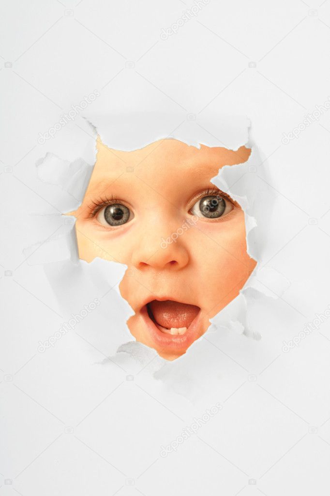 Smiling little girl looking through the torn paper hole
