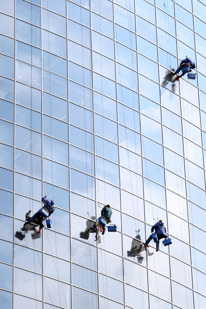 Four workers washing windows in a modern office building