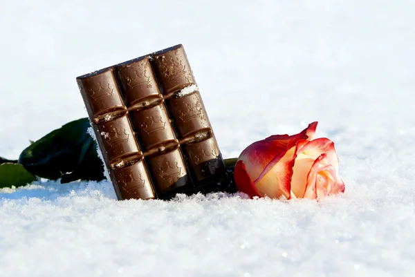 Ein Schokoriegel im Schnee mit einer Rose — Stockfoto