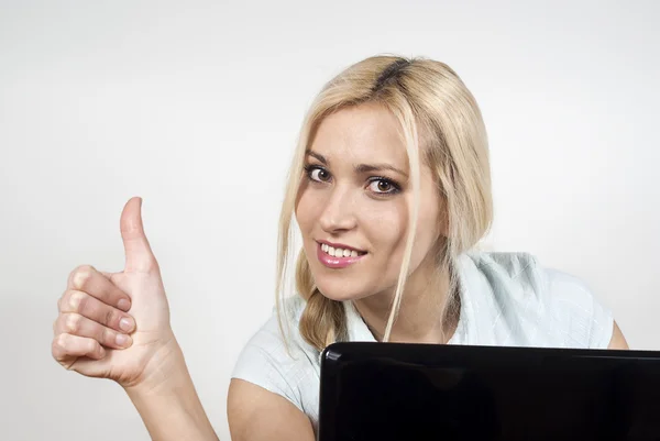 Beautiful happy girl sitting at a laptop computer and displays o — Stock Photo, Image