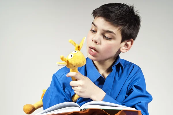 Мальчик читает книгу с игрушкой на заднем плане — стоковое фото