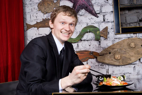 Un chico guapo en el restaurante feliz comiendo sushi — Foto de Stock