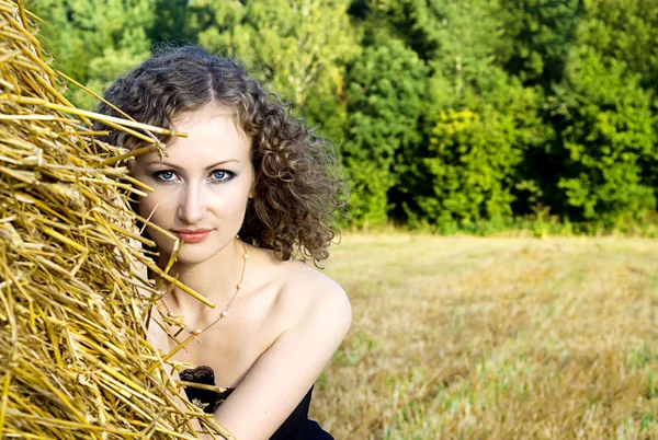Beautiful curly girl near the sheaf of hay in nature — Stock Photo, Image