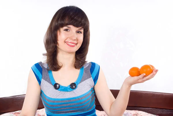 Schöne Mädchen sitzt auf dem Bett und hält Mandarinen — Stockfoto