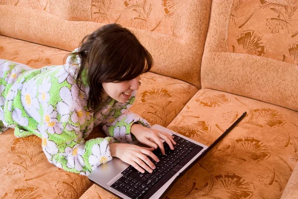 Girl in a bathrobe running a laptop on the couch — Stock Photo, Image
