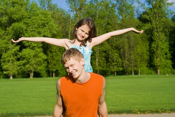 Der Vater hält die Tochter auf dem Rücken, in der Natur — Stockfoto