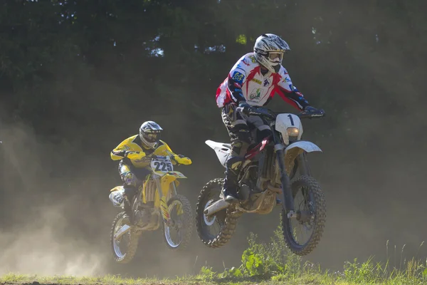 Dwóch zawodników skakać z motocyklem. ciemnym tle. — Zdjęcie stockowe