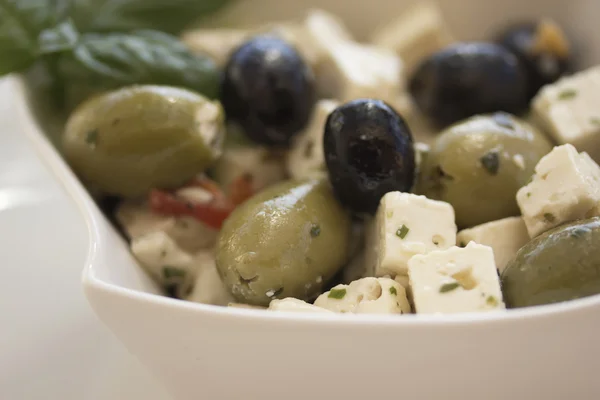 Salat af oliven, serveret med stykker ost i en hvid skål . - Stock-foto