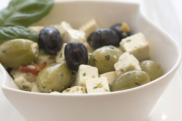 Salat af oliven, serveret med stykker ost i en hvid skål . - Stock-foto