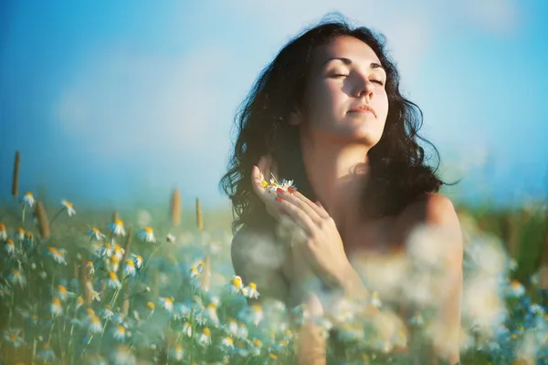 Brunet woman enjoing camomiles in a meadow — Stock Photo, Image