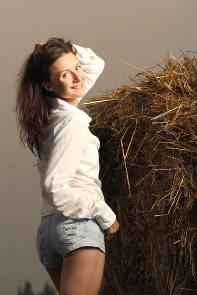 Charming young smiling woman posing near the haystack — Stock Photo, Image
