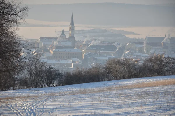 Uitzicht vanaf besneeuwde heuvel naar de kleine stad vroeg in de ochtend — Stockfoto