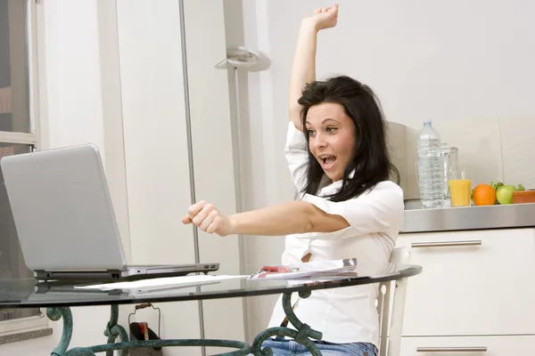 Жінка працює на ноутбуці, піднімаючи руку в знак успіху — стокове фото