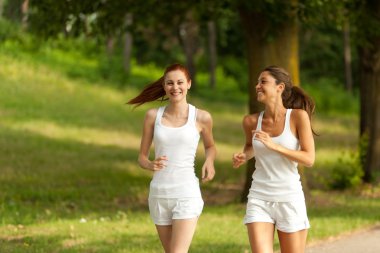 Two young woman running in a park clipart