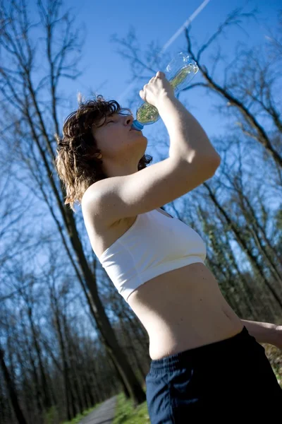 genç bir beyaz kadın spordan sonra açık havada içki içer.
