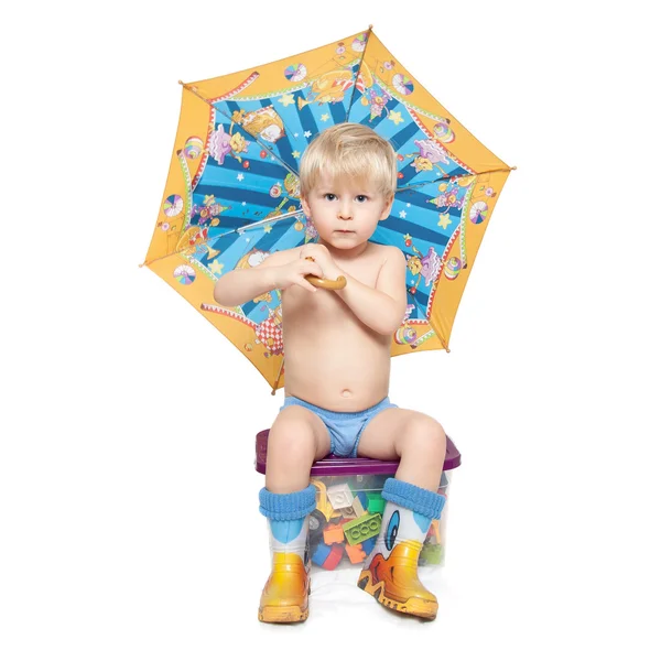 De jongen onder een paraplu zit op een doos Stockfoto
