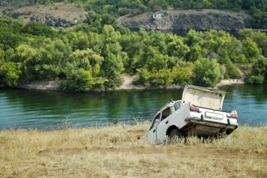 Abandoned car on the riverbank near the water clipart
