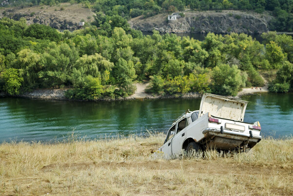 Abandoned car on the riverbank near the water