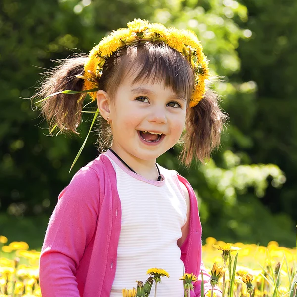 A smiling girl sitting on the dandelion field with the dandelion — Stock Photo, Image
