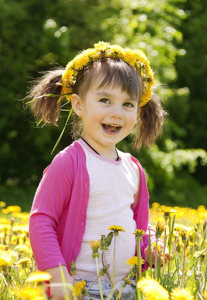 A smiling girl sitting on the dandelion field with the dandelion — Stock Photo, Image