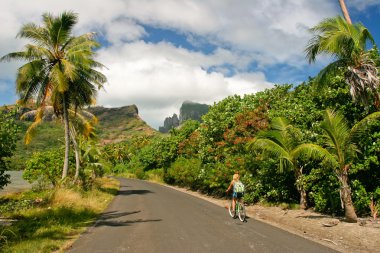 Girl riding a bicycle through the tropical island Bora Bora , French Polynesia clipart