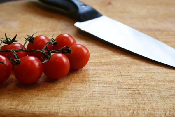 Pomodori ciliegia su un tagliere con coltello Immagine Stock