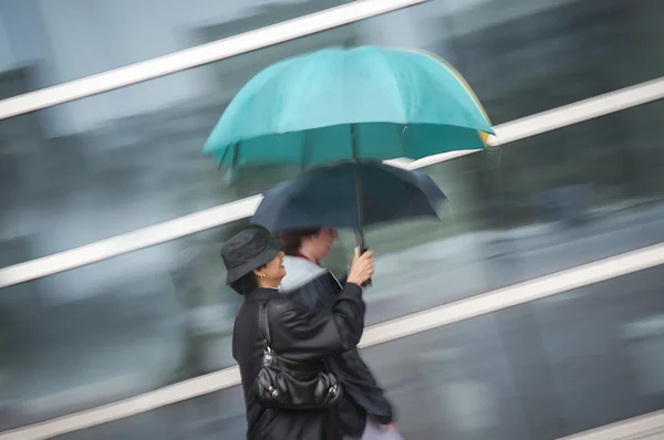 Två kvinnor under paraply i regn Royaltyfria Stockbilder