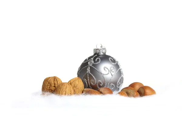 A silver Christmas tree ball and nuts in the snow as a close up view — Stock Photo, Image
