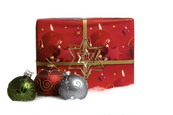 Tre julgranskulor och ett stort rött gåva paket i snön — Stockfoto