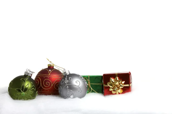 Three Christmas baubles and two small gift packet in the snow — Stock Photo, Image