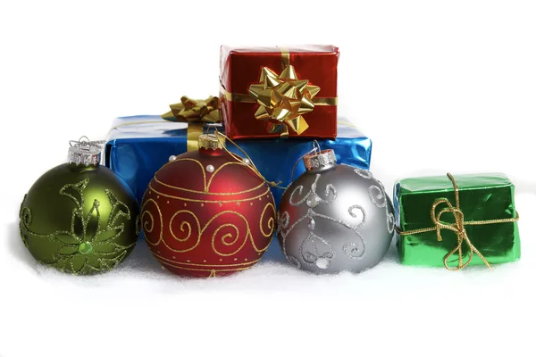 Three Christmas baubles and some gift packages in the snow — Stock Photo, Image