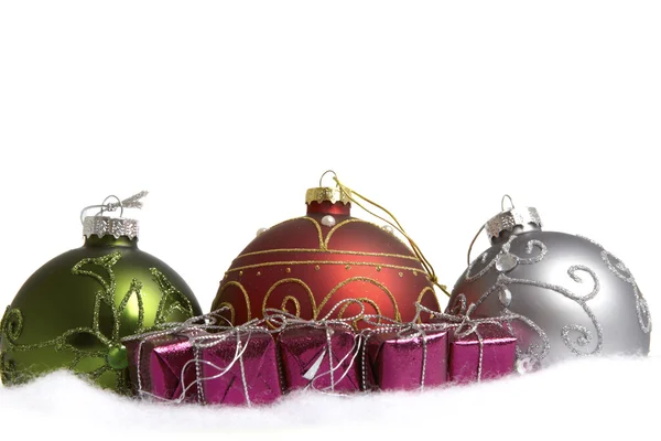 Tre julgranskulor och några små presentförpackningar i snön — Stockfoto