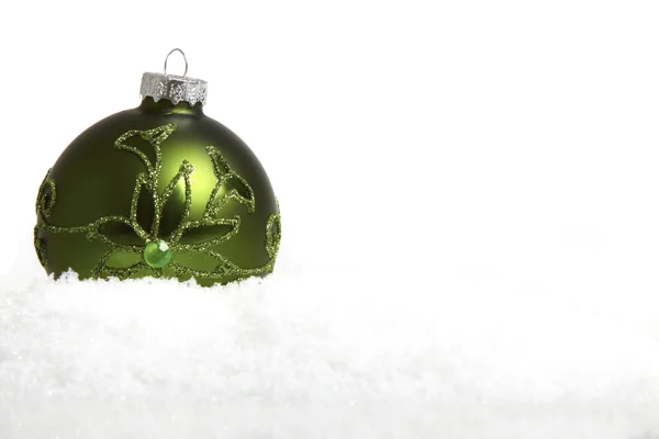 A green Christmas tree ball in the snow as a close up view — Stock Photo, Image