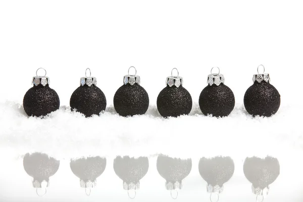 Seis pequeñas bolas de árbol de navidad negro en la nieve espejada, sobre fondo blanco — Foto de Stock