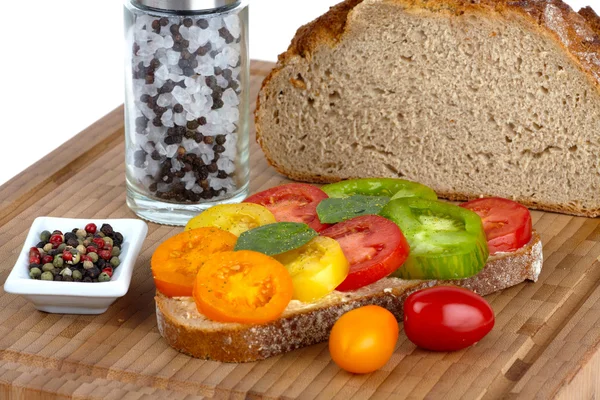 stock image Several sliced organic tomatoes in a bowl with a cup of peppercorns and spring onions on a bamboo cutting board