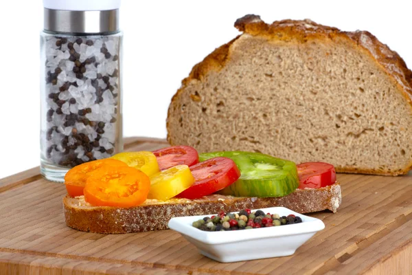 Stock image Several sliced organic tomatoes in a bowl with a cup of peppercorns and spring onions on a bamboo cutting board