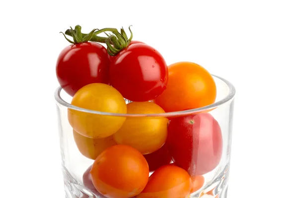Un verre rempli de petites tomates biologiques colorées devant fond blanc — Photo