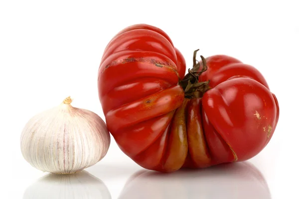 Large red giant beefsteak tomato with garlic mirror in front of white background — Stock Photo, Image
