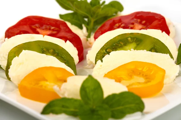 Sliced tomatoes and mozzarella with basil on a plate in front of white background — Stock Photo, Image