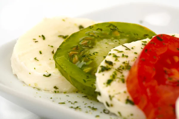 Geschnittene Tomaten und Mozzarella mit Olivenöl und Kräutern auf einem Teller vor weißem Hintergrund — Stockfoto