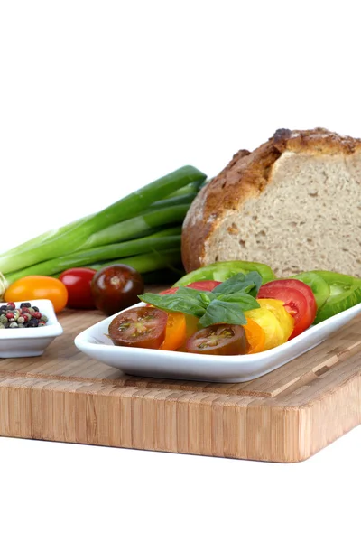 stock image Several sliced organic tomatoes in a bowl with a cup of peppercorns and spring onions on a bamboo cutting board