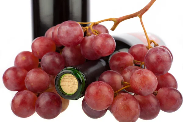 Uvas vermelhas colocadas em uma garrafa de vinho no fundo branco — Fotografia de Stock