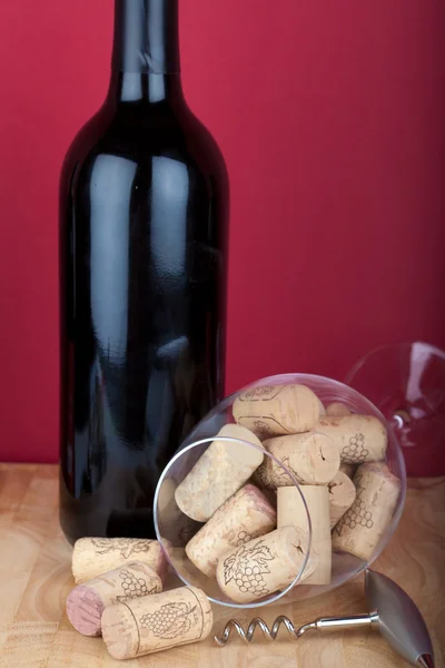 Copo de vinho cheio de rolhas na frente de uma garrafa de vinho com um saca-rolhas — Fotografia de Stock