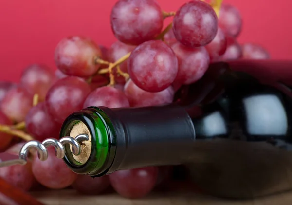 Μπουκάλι κρασί με τιρμπουσόν είναι μπροστά από κόκκινα σταφύλια — Φωτογραφία Αρχείου