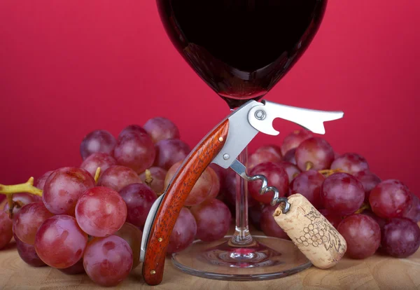 Un cavatappi con sughero davanti a un bicchiere di vino rosso — Foto Stock